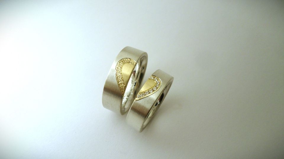 Zilveren relatieringen met gouden 'half' hart. Damesring gezet met 9 diamantjes, en de herenring bewerkt. Samen vormen ze een 'heel' hart. 4 en 5 mm breed. Goudsmid Hans Rietman